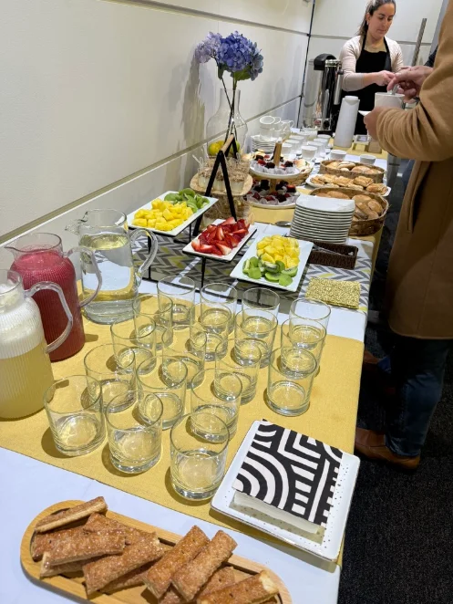 Estación de bebidas y comida con jugos, vasos y bandejas de fruta