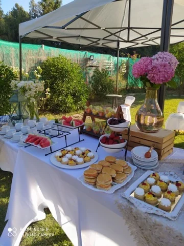 Montaje al aire libre bajo toldo, con flores y mesa de dulces