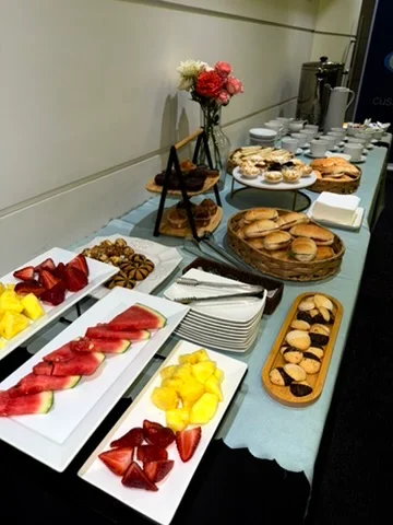 Mesa larga con bandejas de fruta fresca, pastelería y arreglo floral